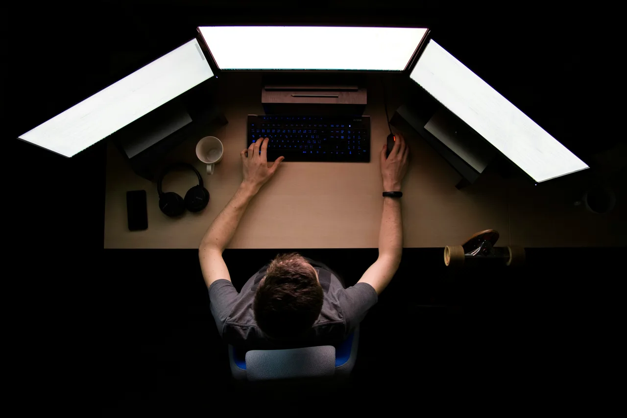 An engineer working at a multi-monitor workstation with a backlit keyboard, seen from above